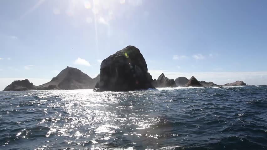 Sihloutte of a jagged rocky islands with clear blue sky and the sun refracting, slight flares. Migrating destination for white shark, whales and sea birds. Southeast Farallon Island, Pacific Ocean. 