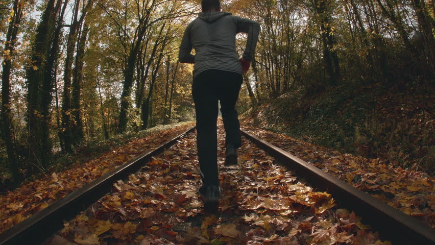 Fisheye pov angle of man jogging down train tracks in fall season.  caucasian male running down railroad covered in autumn leaves with wide  point of view