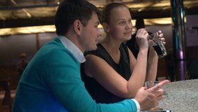 Slow motion clip of a young man and woman sitting at the bar counter in cafe or club. Happy and relaxed people having drinks