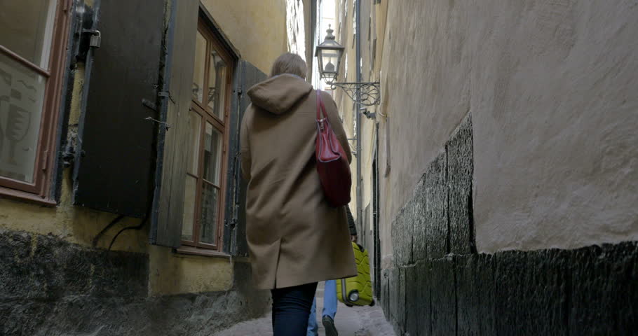 Steadicam shot of make and female tourists walking in Marten Trotzigs Grand, the narrowest street of Stockholm. Woman using cellphone to take picture of old grungy houses