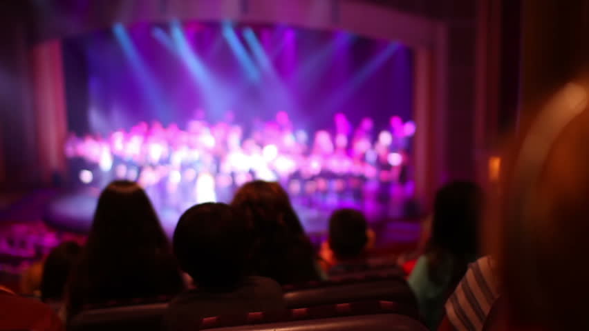 Audience members applaud at a stage show.