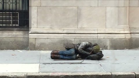 NEW YORK - NOV 13, 2015: homeless man sleeping in the street while woman on cell phone passes by in NY. Homelessness is still a major problem in New York City.