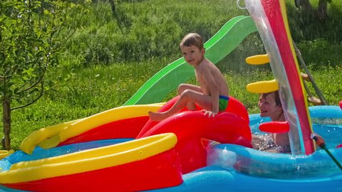 Kid sliding down on inflatable water pool. Two boys having fun in air pool with water, a slide in between. Pool on grass.
