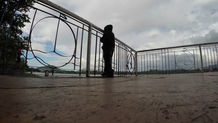 Little boy viewing the lake at shore deck boardwalk railings. Silhouettes