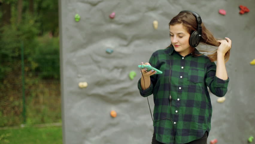 Girl standing againt climbing wall and listening music on headphones
