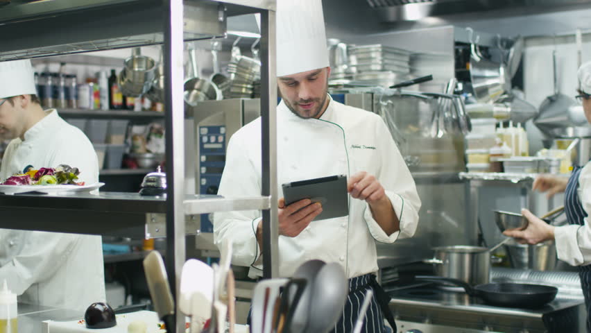 Professional chef in a commercial kitchen in a restaurant or hotel is using a tablet computer. Shot on RED Cinema Camera in 4K (UHD).