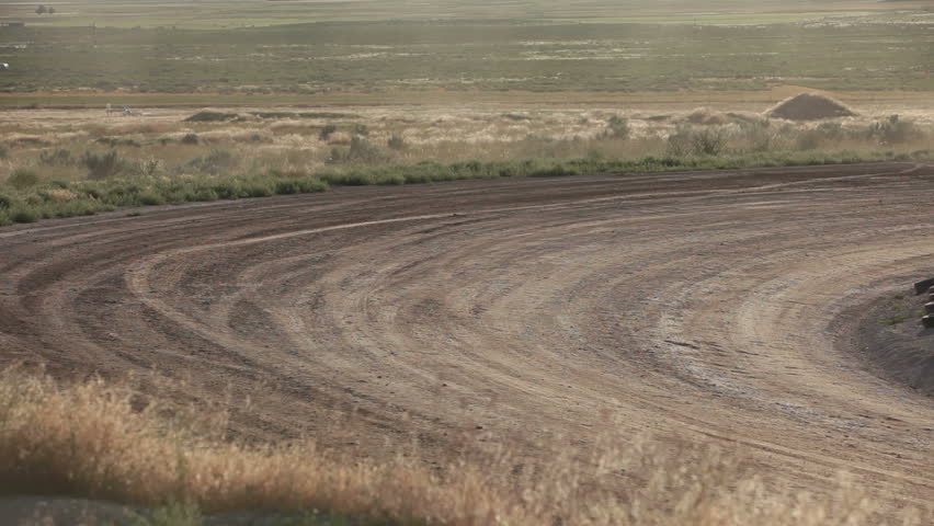 Race cars high speed on dirt oval course. Highly modified stock cars driving and racing on a very dirty and dusty track corner. High speed around dusty corner towards view.