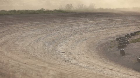 Race cars on dirt oval course spread out following each other. Highly modified stock cars driving and racing on a very dirty and dusty track corner. High speed around dusty corner. 