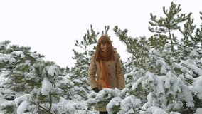 Young woman with red hair in warm clothes, throws up the snow from the trees, covered with white snow.