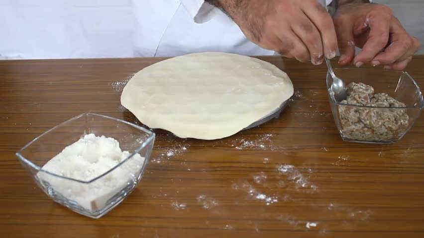 Two men working together preparing dough on wooden table covered with flour, showing teamwork and traditional baking process in a cozy kitchen environment.