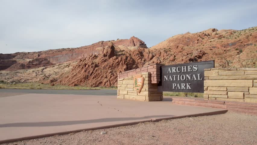 Woman walks towards Arches National Park Entrance Sign Moab Utah USA