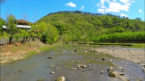 Beautiful view of river flows near village with green forest on the hill under sky with white clouds, Georgia, Guria