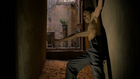 Skinny scary man dancing in a narrow hallway without a shirt.
