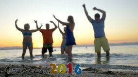 Slow motion clip of happy family members enjoying holiday on the shore. They dancing in shallow sea water at sunset and celebrating New Year 2016