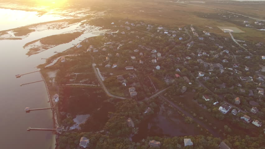Slow aerial pan of Ocracoke Island with a beautiful sunrise glow and lens flare.