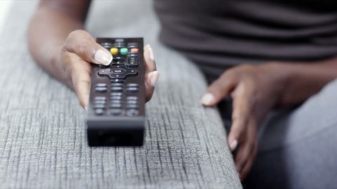Young woman on sofa at home, changing tv channel with remote control