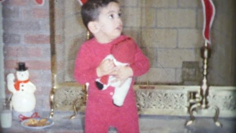MADISON, WISCONSIN, DECEMBER 25, 1963: A cute little boy wearing red pajamas enjoys opening his presents on Christmas Day in 1963.