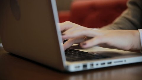Female hands working on laptop in cafe and drinking coffee