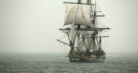 A tall sailing ship schooner sails on the high seas in misty fog.
