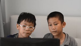 2 Asian kids who are friends having fun playing on a laptop computer playing video games on a website