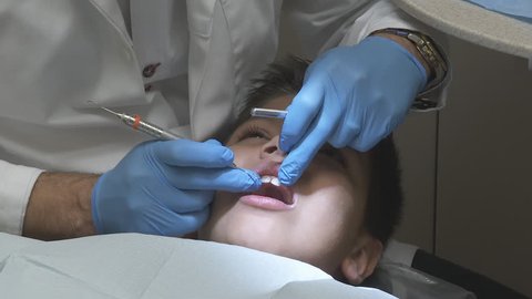 Dental Check Up On Kid - A male adult dentist performs a regular dental exam checkup on a young boy's teeth