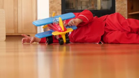 A cute little boy in his pajamas plays with his toy airplane on the hard wood floor in the living room