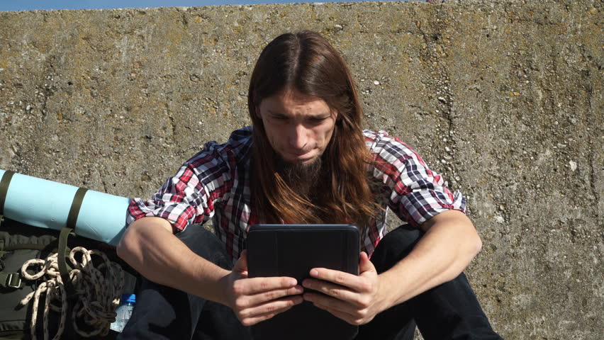 Man tourist backpacker sitting with tablet on wall outdoor 4K"