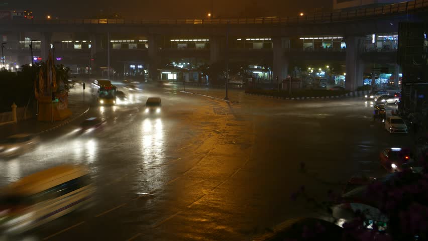 Night traffic at big roundabout, rainy weather, smooth timelapse shot. Dark environment, bright headlight and vehicle traces, quick motion at curving trajectory. Several cars waiting for green light