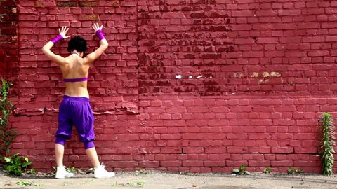 Flexible girl dances near red brick wall at summer day