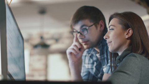 Young man and woman are working on a computer in a loft while discussing a project. Shot on RED Cinema Camera in 4K (UHD).