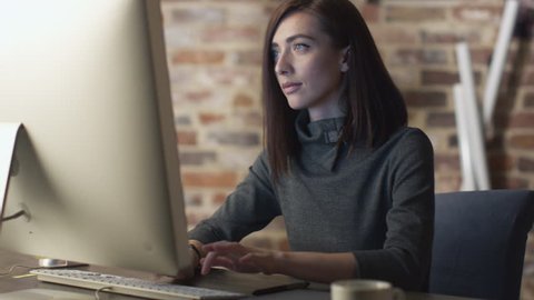 Young brunette woman is working in front of a monitor in a loft. Shot on RED Cinema Camera in 4K (UHD).