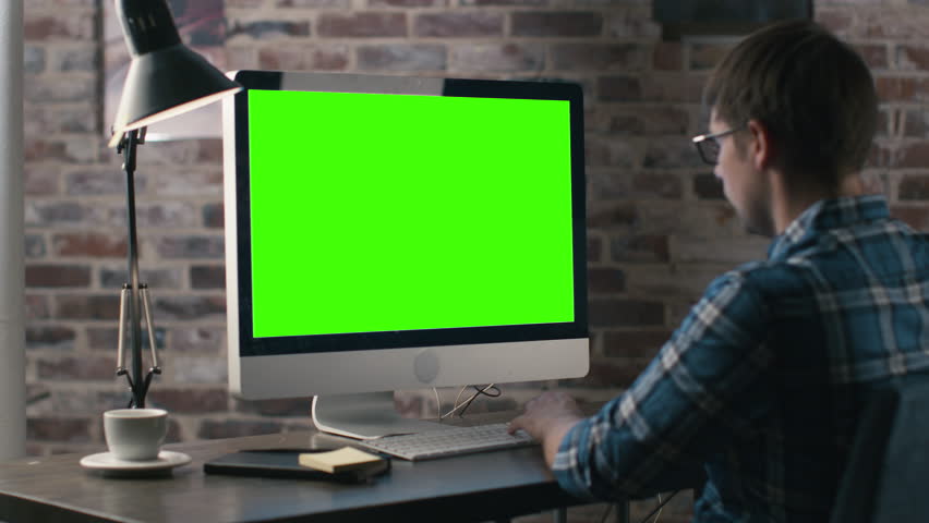 Young man is working on a computer with a mock-up green screen. Shot on RED Cinema Camera in 4K (UHD).
