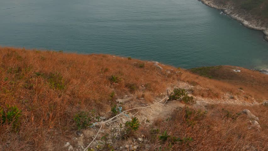 Look down from from deserted hill peak, trampled track downhill, small Ap Lei Pai island and misty horizon line backlit by bright sun light. Ap Lei Chau island mountain peak. Rocky and sandy pathway