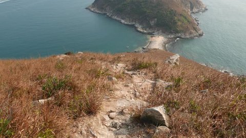 POV walk along rural hill trail, stone and dry grass, fine seascape perspective downward. Ap Lei Chau hike at deserted paths, daytime, first person view camera come forward. Small Ap Lei Pai island