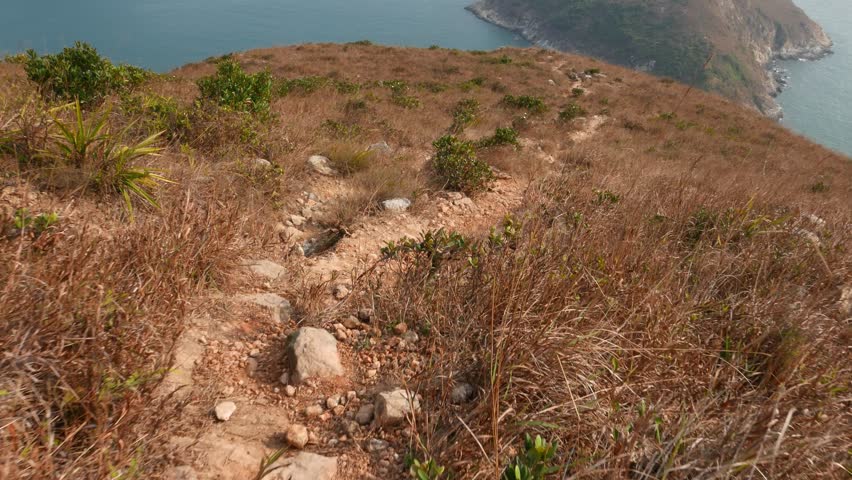 Dangerous climb down of wild track. Path lie down from Ap Lei Chau island peak to coastline and beach. Empty and wild place, rocky slope, rare green bushes, dried brown grass, sandstone dust