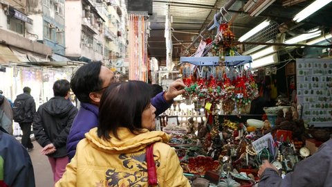 HONG KONG - FEBRUARY 09, 2015: Open street market at inner-city area. Man and woman looking up at hanging talismans, choosing which one to buy