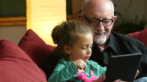 Grandfather sharing an ipad/tablet with his little granddaughter