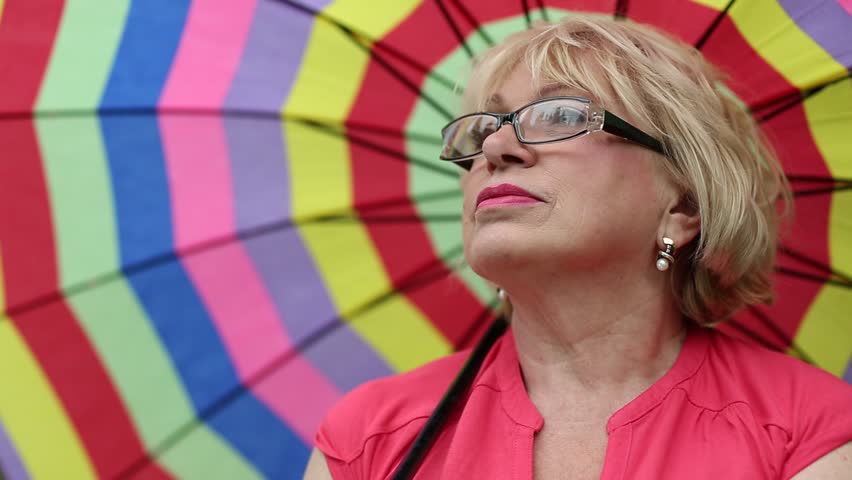Blonde woman in glasses with colorful umbrella looking into the distance
