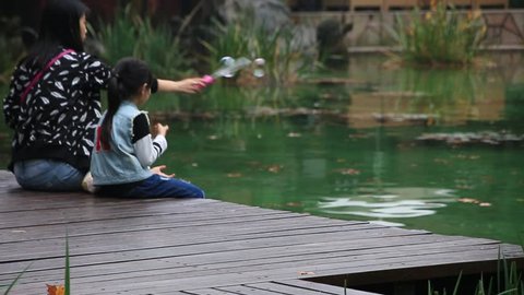 SHANGHAI_07 NOV. 2015 : Mother and daughter sitting and blowing bubbles in Shanghai park, China 