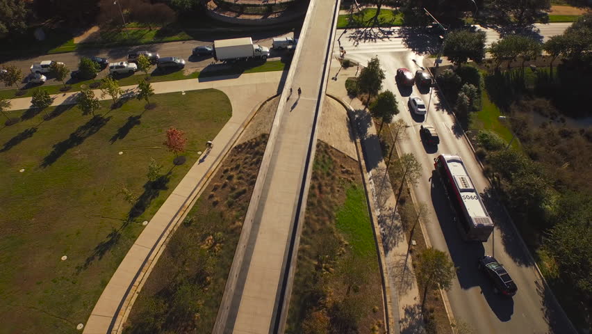 The camera follows the length of the Lamar Pedestrian bridge in Austin, TX, following a bicyclist as the camera tilts up to reveal Lamar Blvd as well as pedestrians and day time traffic.