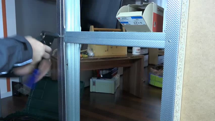 A man holding a metal profile with a riveting tool.