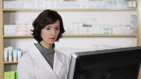 Attractive young woman pharmacist working on her computer in the pharmacy checking information online, videoclip de stoc