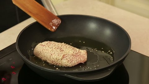 Chef is frying sesame breaded chicken breast on a pan