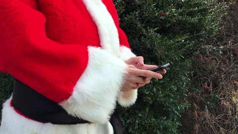 Santa Claus in a red suit online shopping for presents on his smartphone
