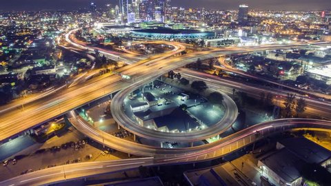 Aerial view of traffic on freeway interchange revealing downtown Los Angeles skyline at night. 4K UHD timelapse.