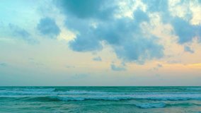 Gentle waves roll and break against a beach. with clouds drifting over a flat horizon in the early morning light. Video 3840x2160