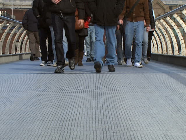 Crowd of adults and teenagers walking across Millennium Bridge, London. 
