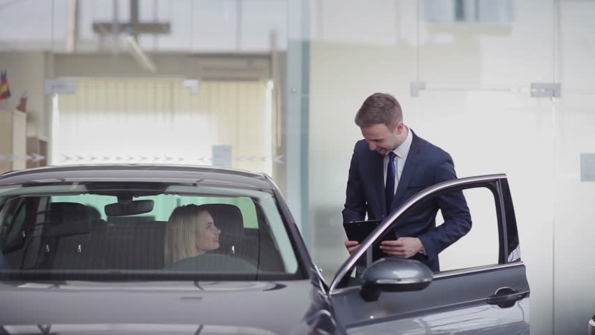Cheerful manager helping girl with choosing car in motor show