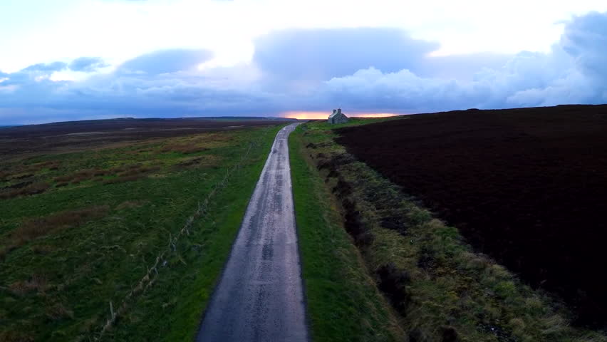 UNITED KINGDOM - CIRCA 2015 - Aerial over a beautiful road through Scotland or Ireland after the rain with distant abandoned stone building.
