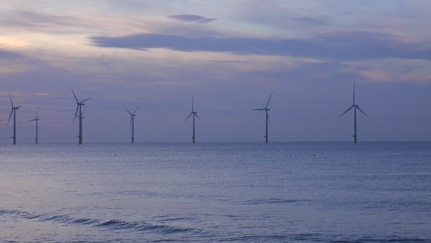 UNITED KINGDOM - CIRCA 2015 - A wind farm generates electricity along a coastline at sunset. | Shutterstock HD Video #13073390